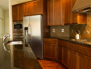 Closeup photo of a walkway behind Kitchen Island with stainless steel appliances, gas stove, stone counter tops and cherry wood cabinets with hardwood floors